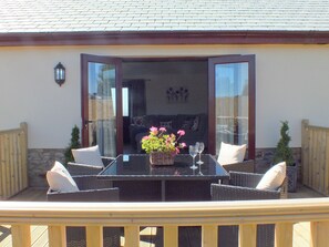 Een terras buiten met een tafel, stoelen, een bloevas en uitzicht op het interieur door glazen deuren.