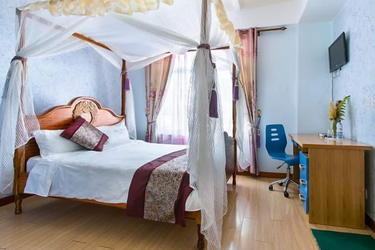 A bedroom with a four-poster bed, a desk, and a television.