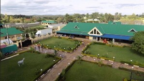 A large, open-air facility with multiple green-roofed buildings, a central paved area, and a zebra statue. - Nice Digital Hotel Mwea (Nairobi)