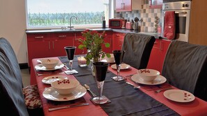Een moderne keuken met rode kastjes, een eettafel gedekt voor zes personen en uitzicht op groen.