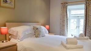 Un letto rifatto con lenzuola bianche, un cuscino a motivi floreali e due lampade da comodino.