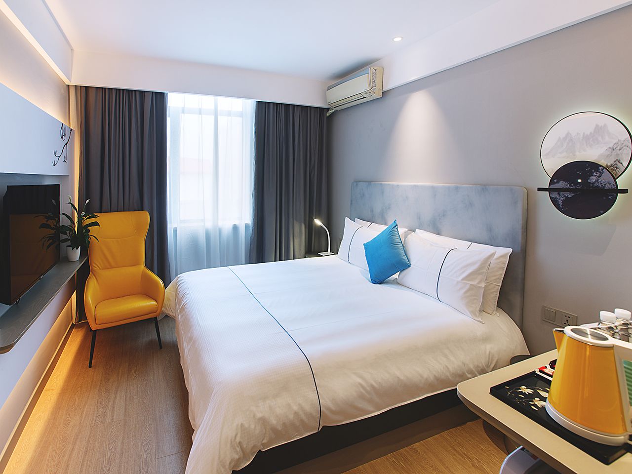 Ein Hotelzimmer mit einem Bett, einem Sessel, einem Nachttisch und einer Wand-Klimaanlage.