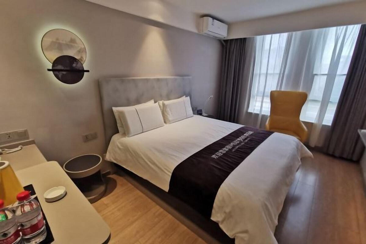 A hotel room with a bed, a chair, a desk, and a wall-mounted air conditioner.