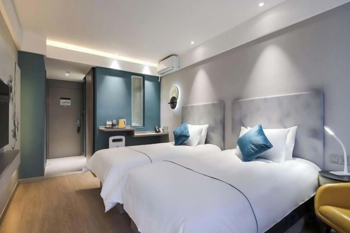 Ett modernt hotellrum med två sängar, ett sängbord, en spegel och ett litet skrivbord med en stol.