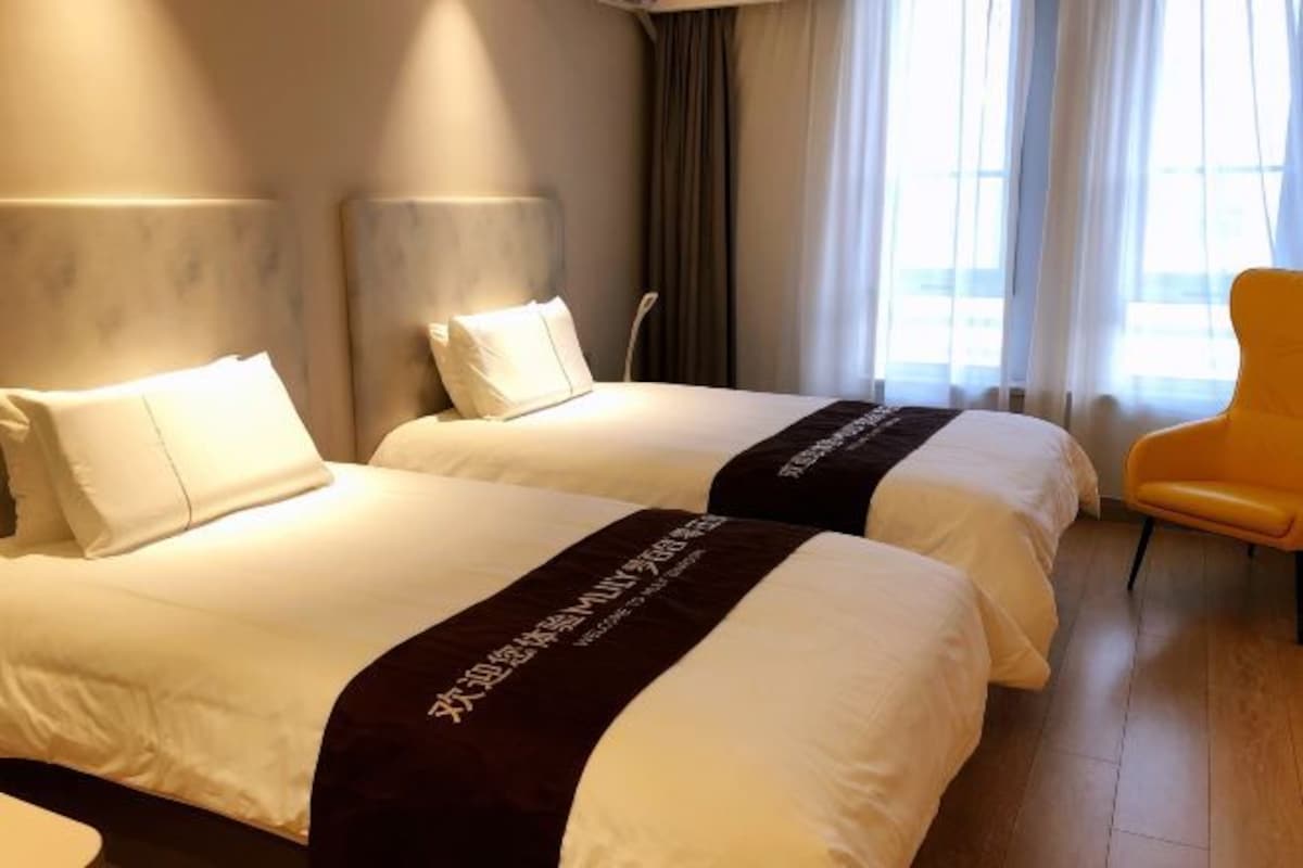 A hotel room with two beds, a chair, and a view of the outdoors.