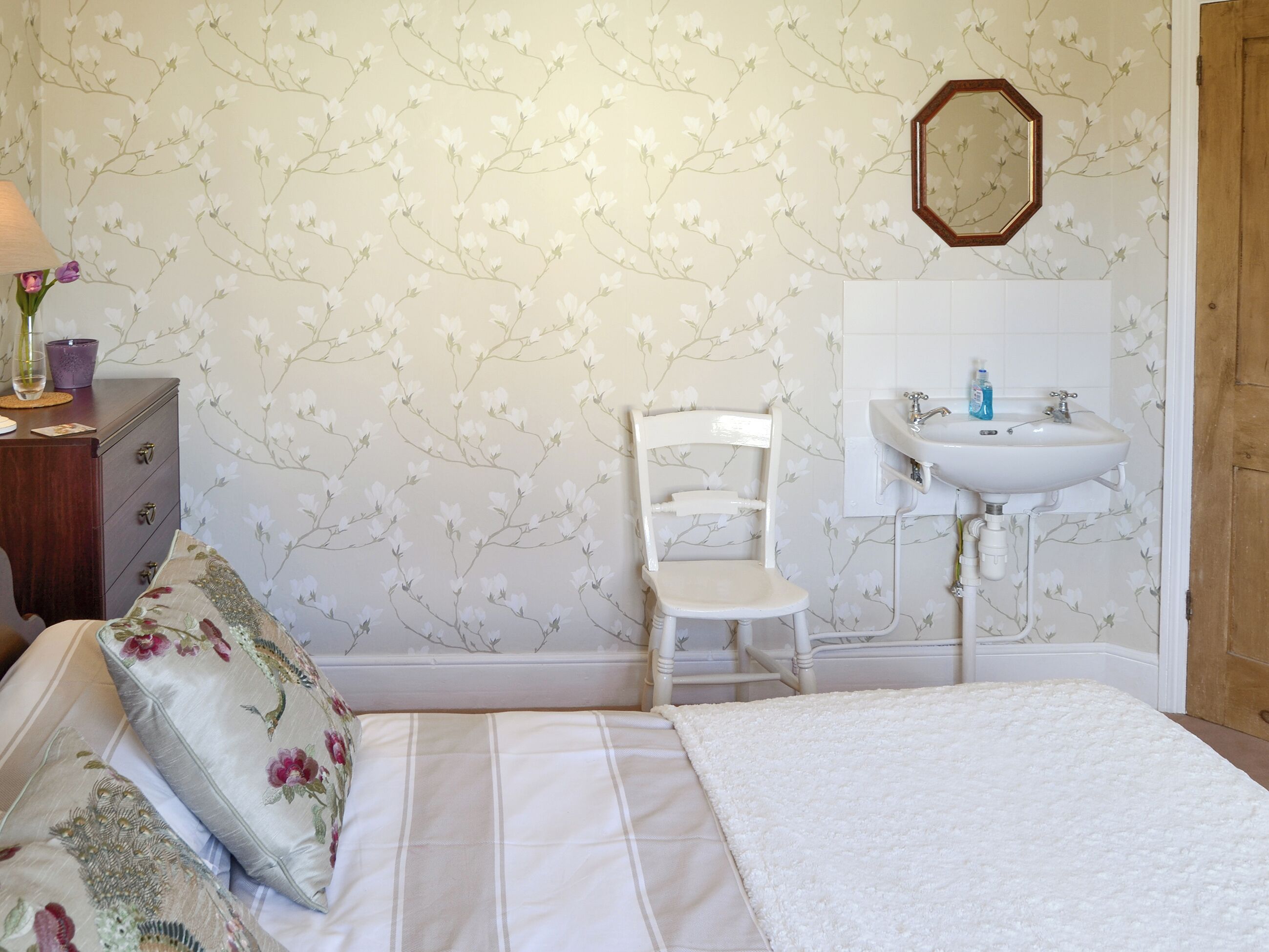 A bedroom with a bed, a dresser, a chair, a white sink, and floral wallpaper.