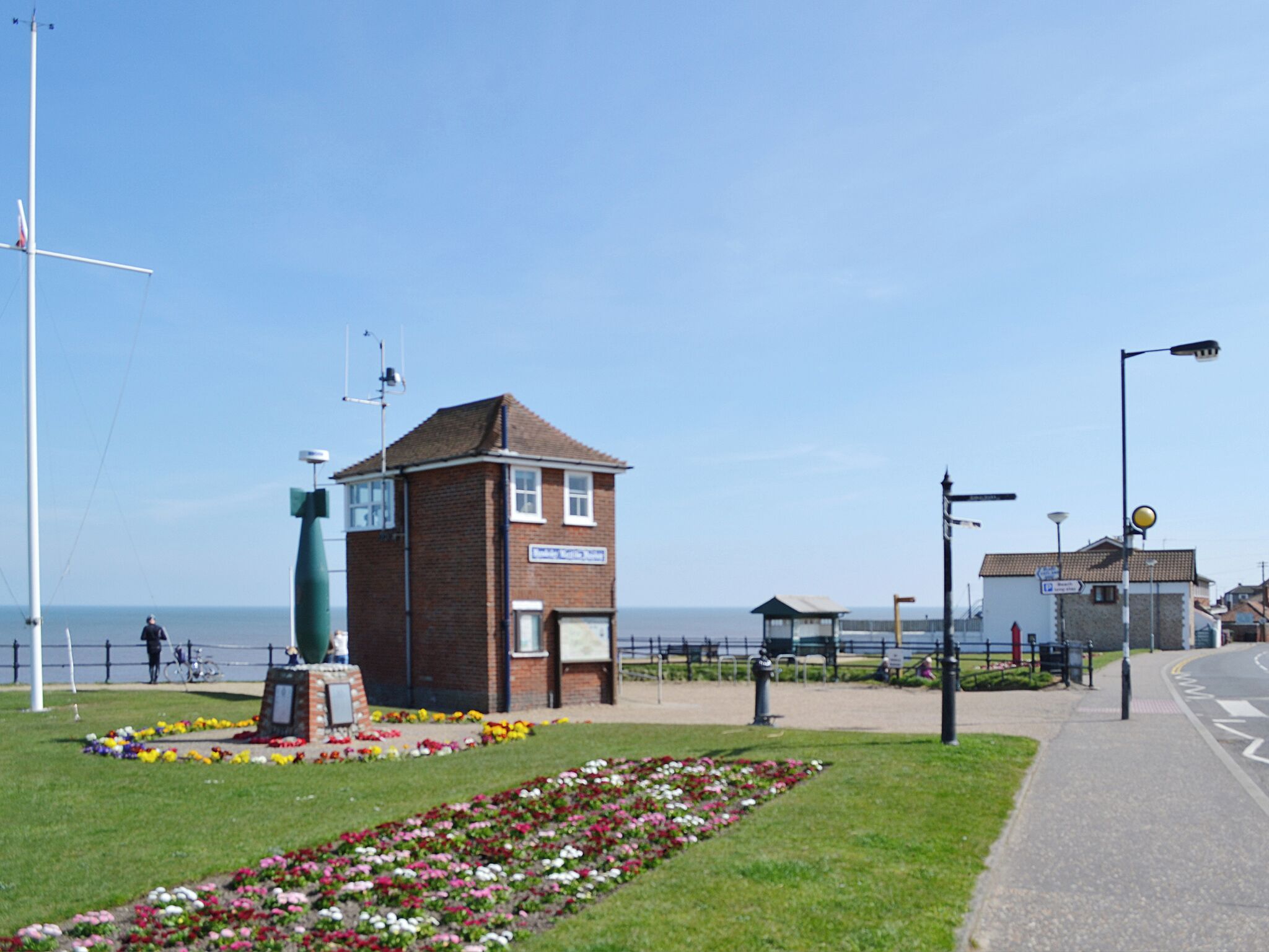 A brick building with a sign, a flower bed, and a view of the sea.