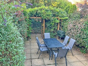 A patio with a table and chairs, surrounded by dense foliage and a wooden pergola. - 5 bedroom accommodation in Mundesley (Mundesley)