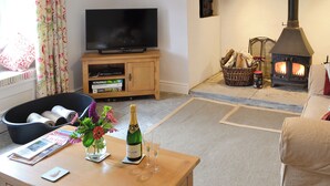 En stue med fjernsyn, et træskab, en pejs, en sofa, et sofabord og en vase med blomster.