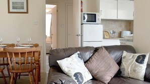A living room with a leather sofa, wooden dining table, and chairs. A white microwave is on the counter, and a framed picture is on the wall. - 2 bedroom accommodation in Bowness-on-Windermere (Bowness-on-Windermere)