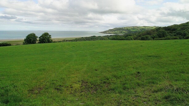 Un campo verde con vista sul mare e sulle colline in lontananza.