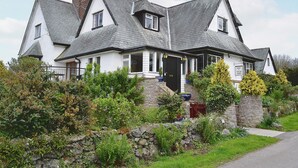 A two-story house with a steeply pitched roof, white exterior walls, and a stone foundation. - 4 bedroom accommodation in Wern-y-Wylan (Wern-y-Wylan)