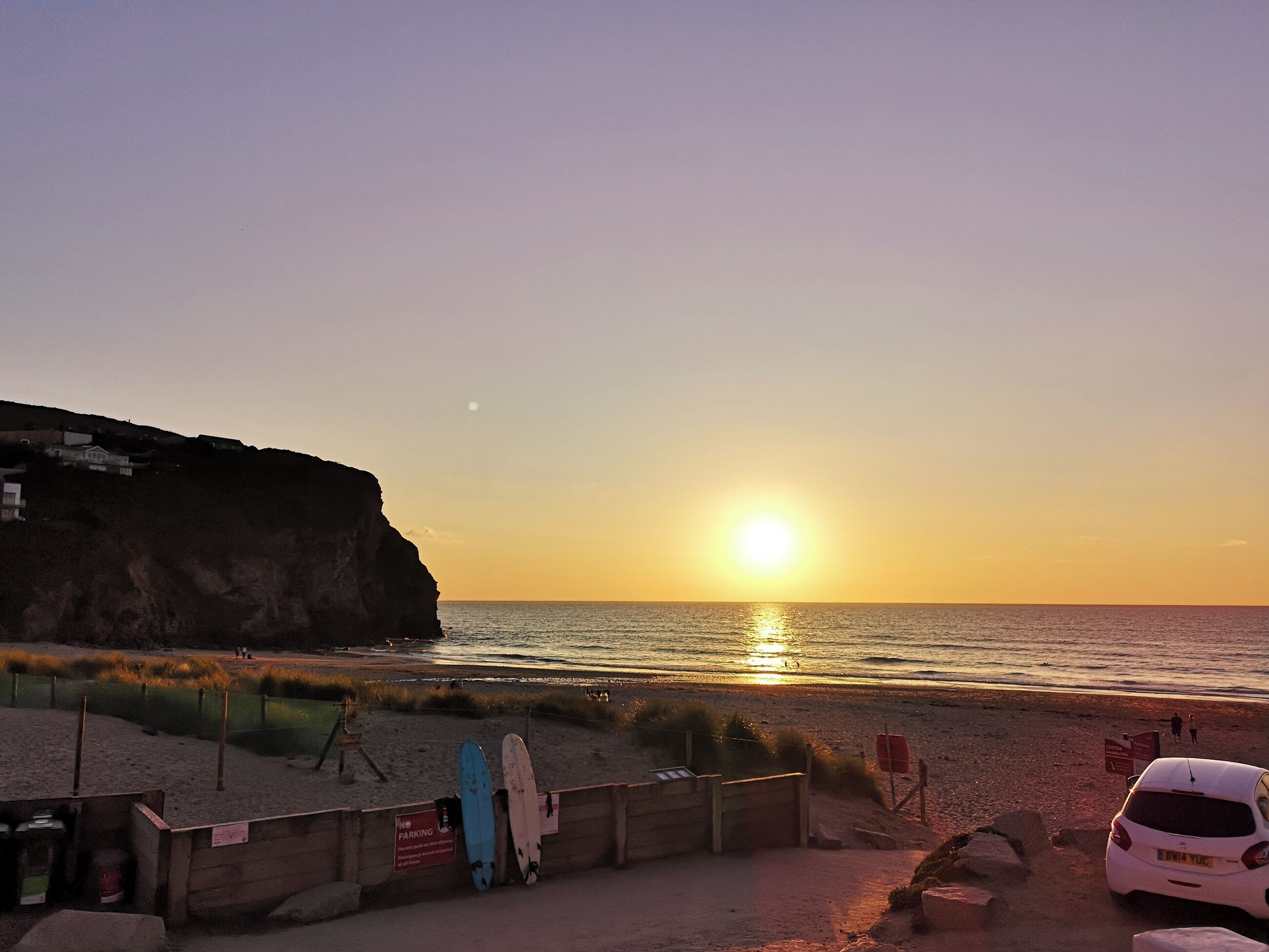 A beach with a sunset, a cliff, and a car parked on the sand.