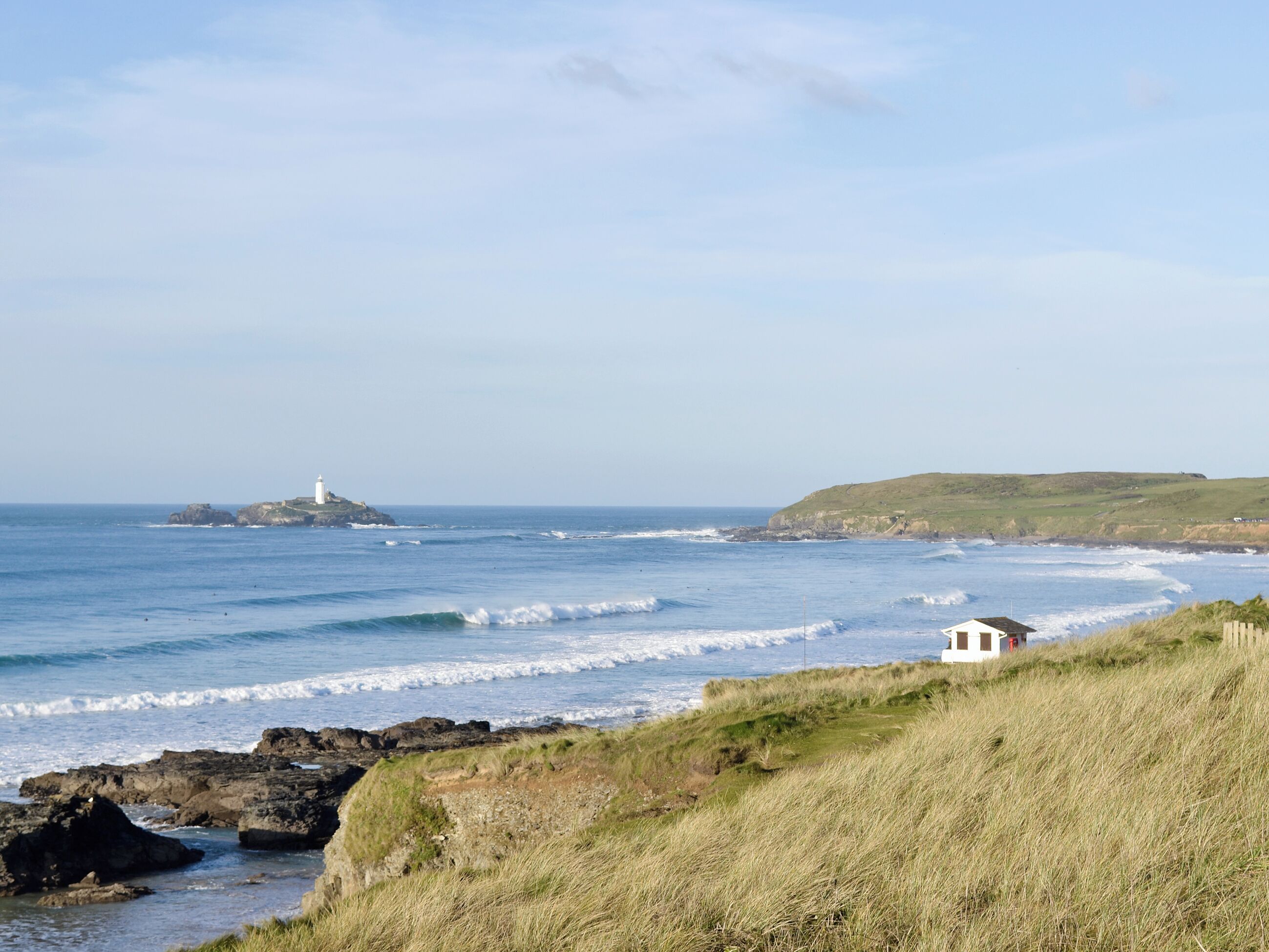 A coastal landscape with a lighthouse, grassy cliffs, and a small white building.