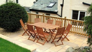 An outdoor patio with a wooden table and chairs, surrounded by a wooden fence and a small garden area. - 4 bedroom accommodation in Portinscale, near Keswick (Portinscale, near Keswick)