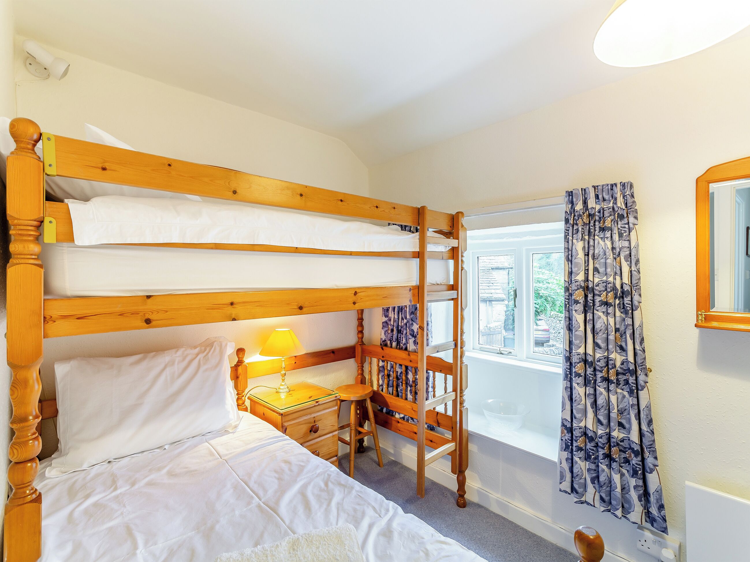 Une chambre avec un lit superposé, un bureau et une lampe, une fenêtre avec des rideaux et un miroir sur le mur.