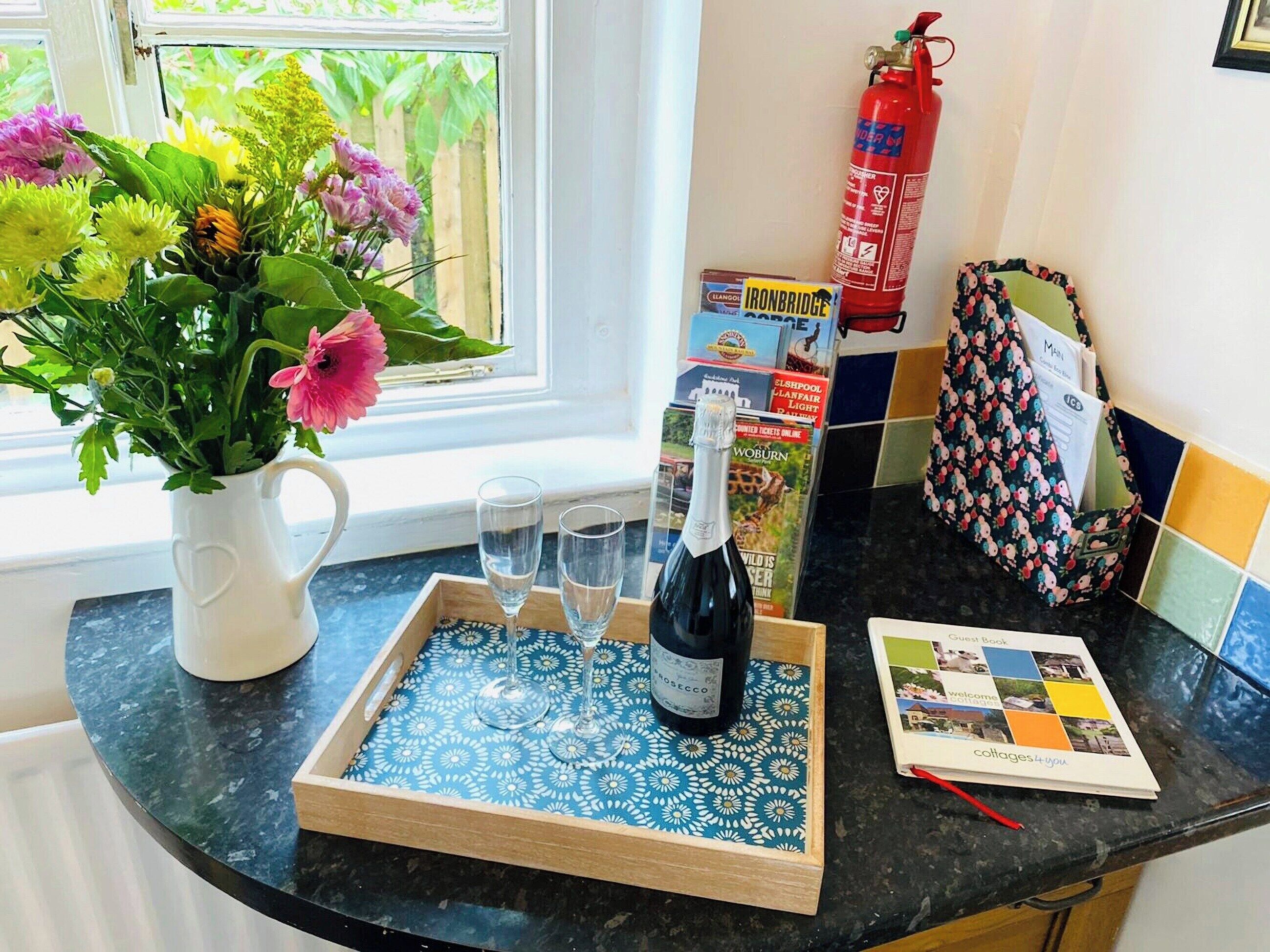 Un comptoir de cuisine sur lequel se trouve un plateau avec une bouteille de vin, deux verres et un bouquet de fleurs.