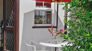 Ein kleiner Patio-Bereich mit einem weißen Tisch und Stühlen, einem roten Sonnenschirm und einem Fenster mit Blumen.