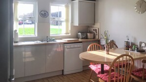 Eine Küche mit Spüle, Geschirrspüler, Fenster und einem Esstisch mit Stühlen.