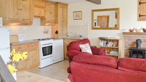 A cozy kitchen with wooden cabinets, a red sofa, a fireplace, and a bookshelf.