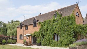 A brick house with ivy covering the walls, a patio with a table and chairs, and a gravel driveway. - 2 bedroom accommodation in Cradley, Malvern (Cradley, Malvern)