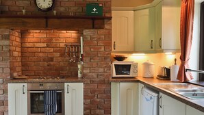 A kitchen with a brick wall, white cabinets, a stove, and a microwave. - 2 bedroom accommodation in Cradley, Malvern (Cradley, Malvern)