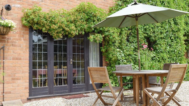 A patio with a table and chairs, a hanging plant, and a brick wall. - 2 bedroom accommodation in Cradley, Malvern (Cradley, Malvern)