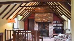 A cozy room with exposed wooden beams, a brick fireplace, a bookshelf, and a floral sofa. - 2 bedroom accommodation in Cradley, Malvern (Cradley, Malvern)