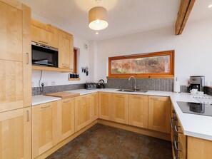 A modern kitchen with wooden cabinets, a built-in microwave, a kettle, and a coffee maker. - 4 bedroom accommodation in Carbost (Carbost)