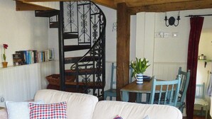 Een gezellige woonkamer met een bank, een houten spiltrap, een eettafel met stoelen en een potplant.