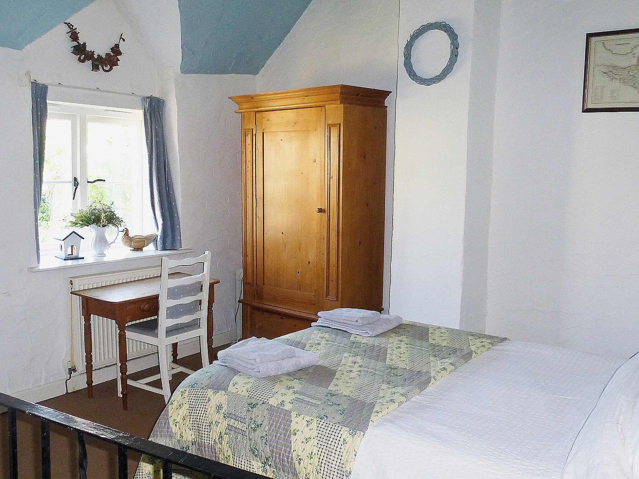 A bedroom with a bed, a wooden wardrobe, a desk with a chair, and a window with curtains.