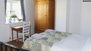 Een slaapkamer met een bed, een houten garderobe, een bureau met stoel en een raam met gordijnen.