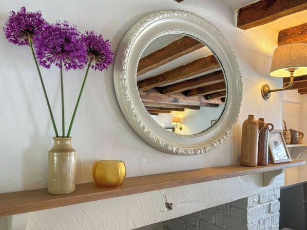 A mirror with a decorative frame, a vase with purple flowers, and a shelf with various items.