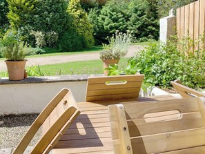 A wooden bench with a backrest and armrests, placed on a patio with a garden view.