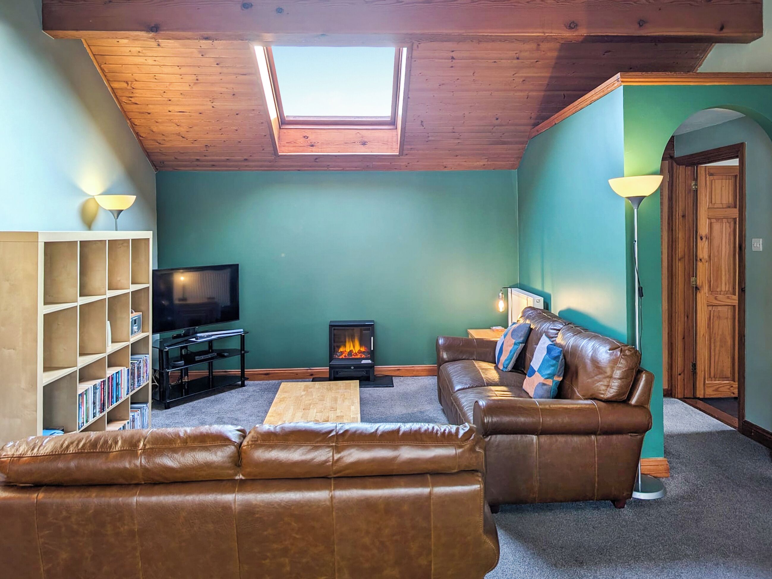 Ein gemütliches Wohnzimmer mit Kamin, Ledersofa, Bücherregal und Fernseher.