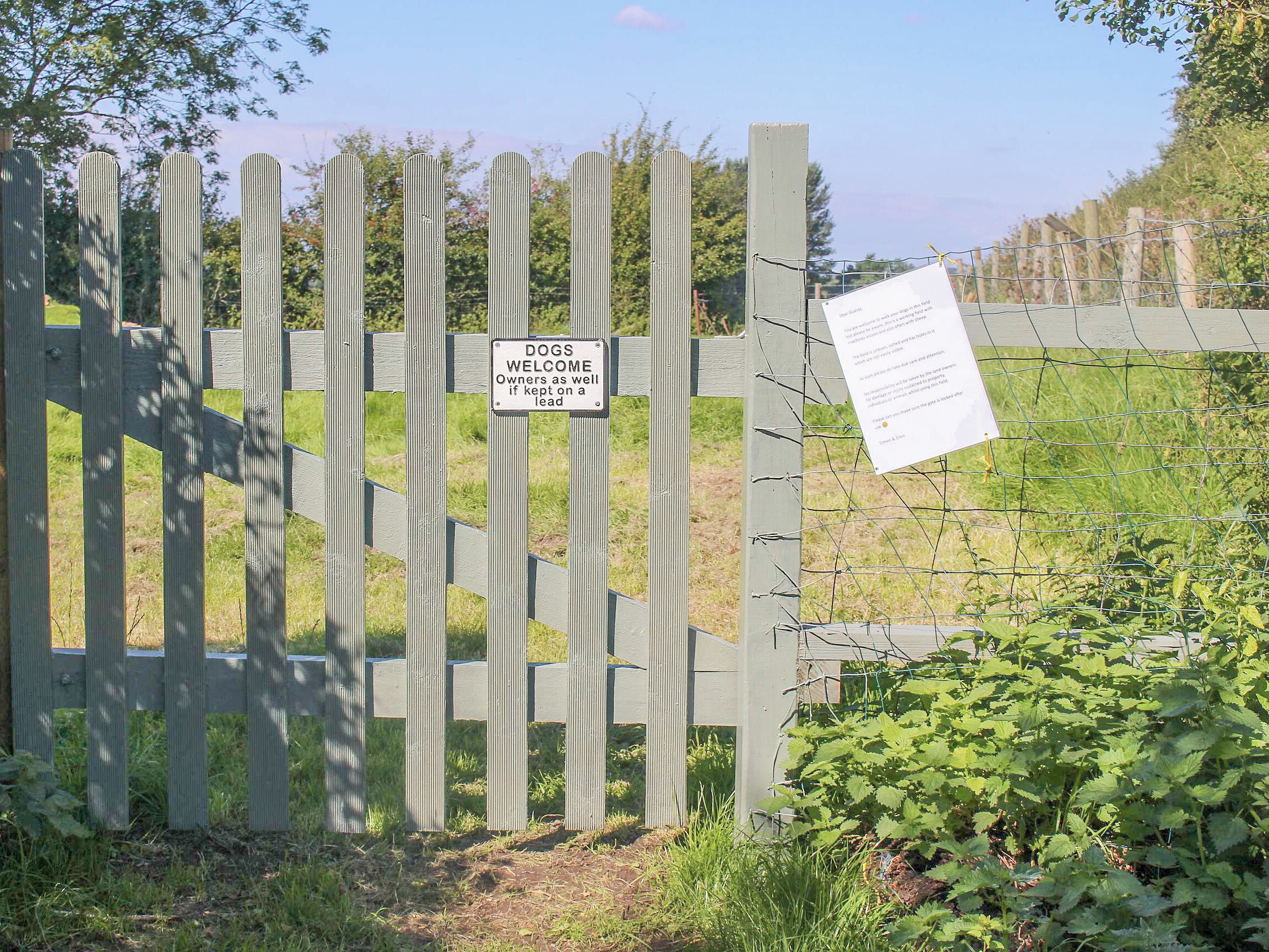 A wooden gate with a sign welcoming dogs and their owners.