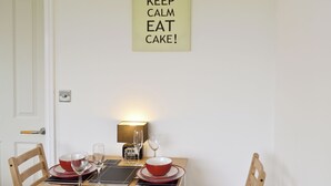 Una mesa de comedor dispuesta con platos rojos y negros, vasos y una vela. Un letrero encima dice "KEEP CALM EAT CAKE!".