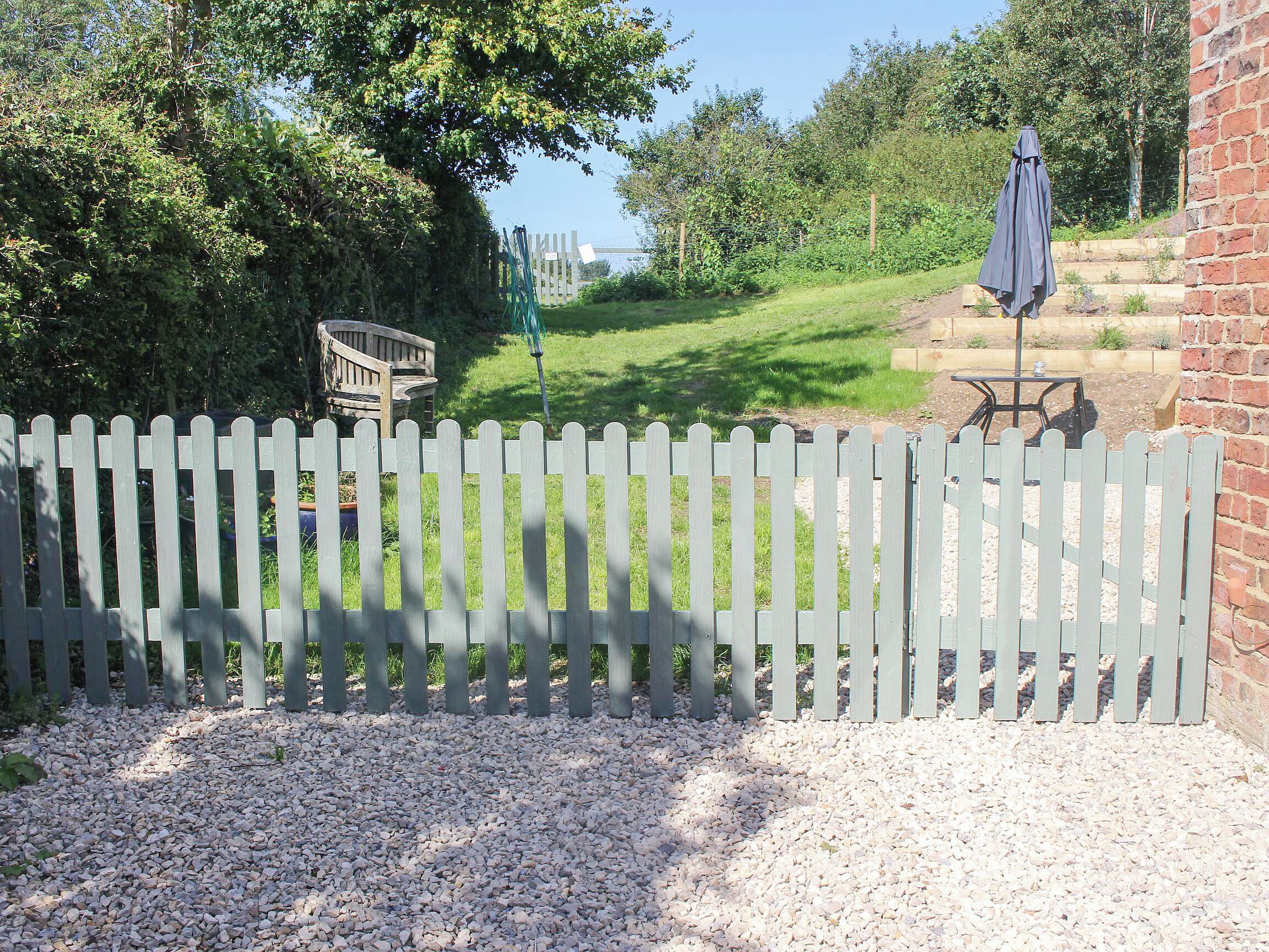 A white picket fence, gravel path, and a brick wall with a table and umbrella.