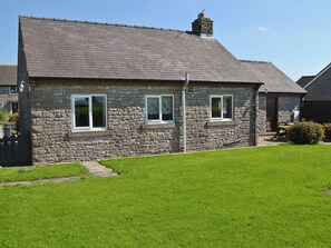 A stone house with a sloped roof, two windows, and a chimney.