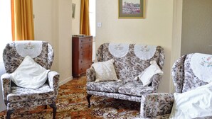 A living room with floral-patterned armchairs and a sofa, a wooden dresser, and a framed picture on the wall. - 2 bedroom accommodation in Skelmorlie, near Largs (Skelmorlie, near Largs)