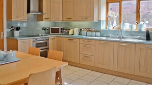 A modern kitchen with wooden cabinets, a built-in oven, a microwave, and a sink with a window above it. - 4 bedroom accommodation in Alvechurch (Alvechurch)