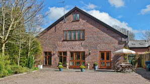 A brick building with a gravel driveway, wooden doors, and a patio area with outdoor furniture. - 4 bedroom accommodation in Alvechurch (Alvechurch)