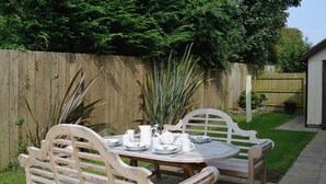 A wooden outdoor table set with plates, cups, and a pitcher, surrounded by chairs. - 4 bedroom accommodation in Marhamchurch, near Bude (Marhamchurch, near Bude)