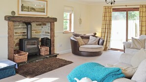 A cozy living room with a stone fireplace, a comfortable sofa, a wooden coffee table, and a bookshelf. - 4 bedroom accommodation in Marhamchurch, near Bude (Marhamchurch, near Bude)