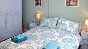 Een slaapkamer met een bed, nachtkastje, lamp, kledingkast en twee aan de muur bevestigde foto's.
