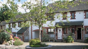 A traditional stone building with a cobblestone courtyard, a central tree, and a small bench. - 2 bedroom accommodation in Buckfastleigh (Buckfastleigh)