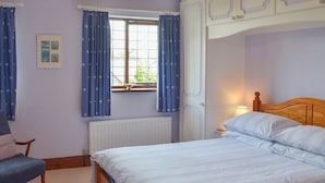 A bedroom with a bed, a chair, a window with curtains, and a radiator. - 2 bedroom accommodation in Buckfastleigh (Buckfastleigh)