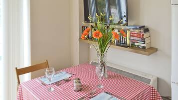 Une table à manger recouverte d’une nappe à carreaux rouges et blancs, un vase rempli de fleurs et une bibliothèque remplie de livres.