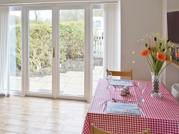 Un comedor con mantel a cuadros, un florero con flores y vistas al jardín a través de puertas de vidrio.