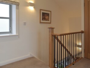 A staircase with wooden handrails and black balusters, a framed picture on the wall, and a window with a white frame and a visible light switch.